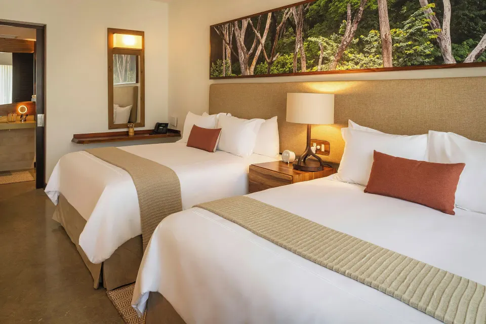 Two double beds with artwork and soft lighting in a guest room at El Mangroove Papagayo