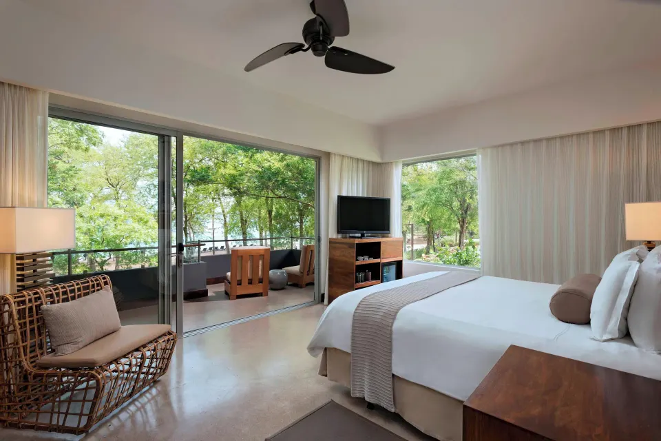 Guest room with king bed and balcony overlooking trees at El Mangroove Papagayo