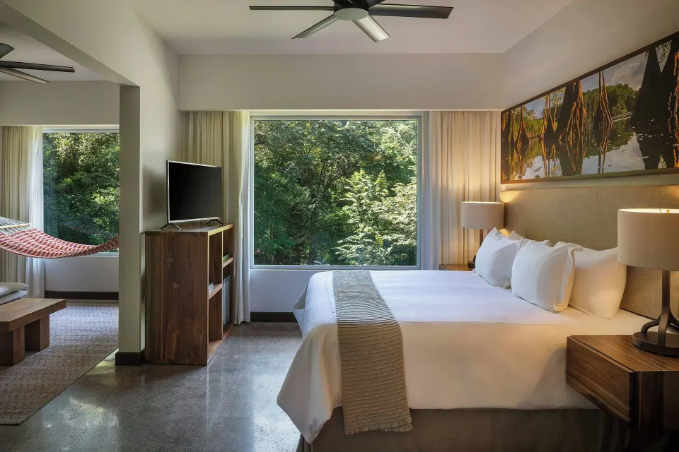 King bed with large forest-view window and hammock seating area at El Mangroove Papagayo