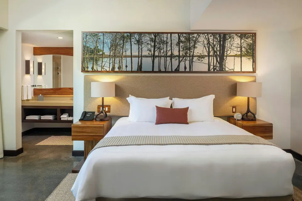 King bed centered with bedside lamps and panoramic nature artwork at El Mangroove Papagayo