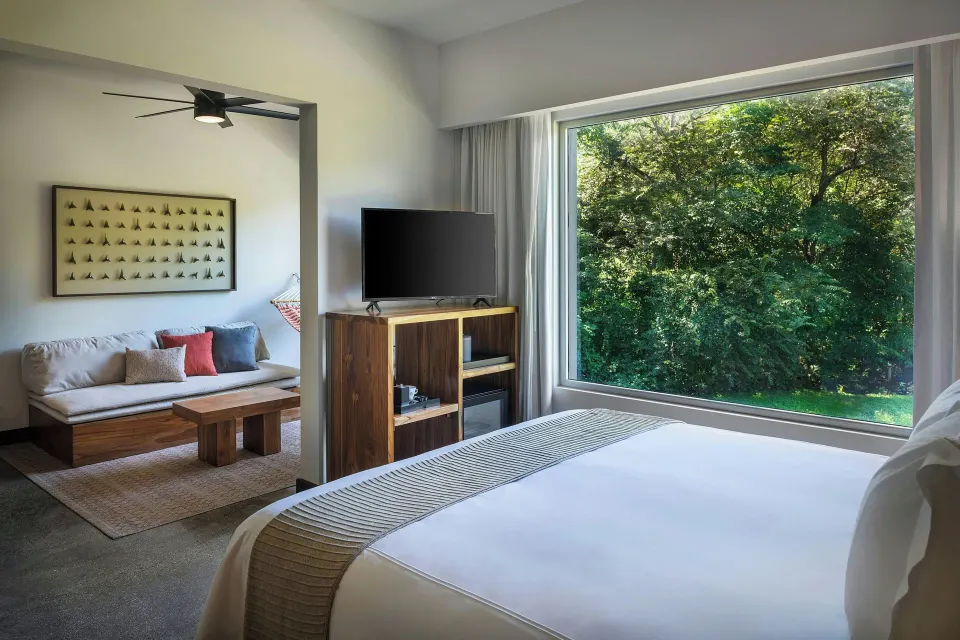 King bed looking toward large forest-view window and sitting area at El Mangroove Papagayo