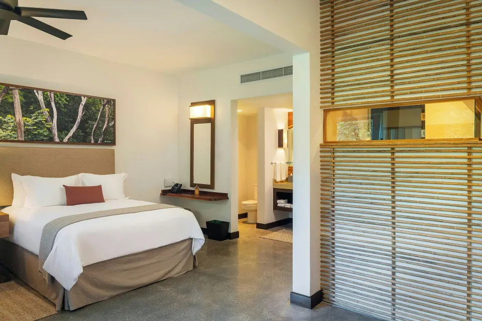 Guest room with king bed and wooden slatted divider at El Mangroove Papagayo