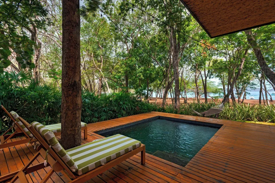Private plunge pool on deck with striped loungers and trees at El Mangroove Papagayo