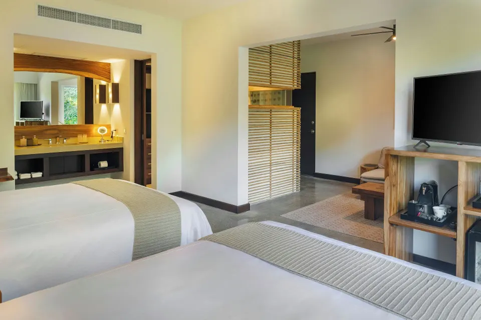 Two beds with TV console and open bathroom in suite at El Mangroove Papagayo