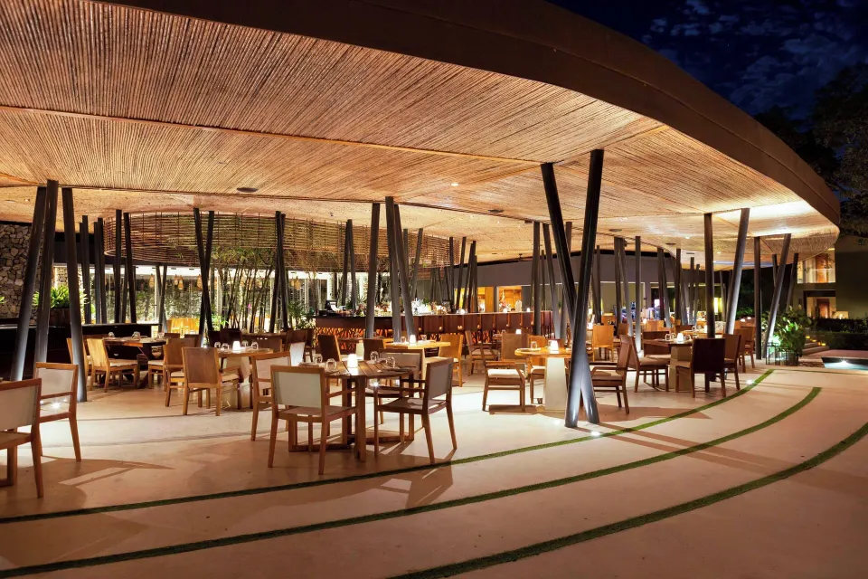 Nighttime view of covered outdoor restaurant seating under a curved canopy at El Mangroove Papagayo
