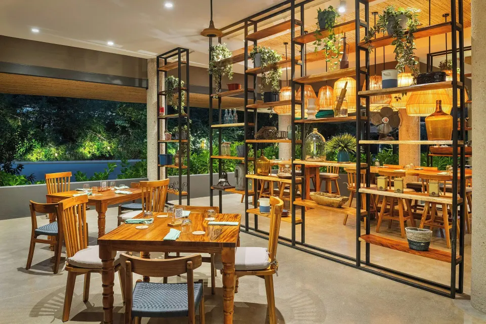Cozy corner of the resort restaurant with wooden tables and decorative shelving at El Mangroove Papagayo