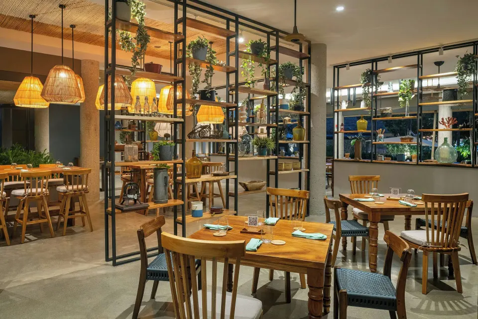 Interior restaurant view with plants on metal shelving and warm pendant lights at El Mangroove Papagayo