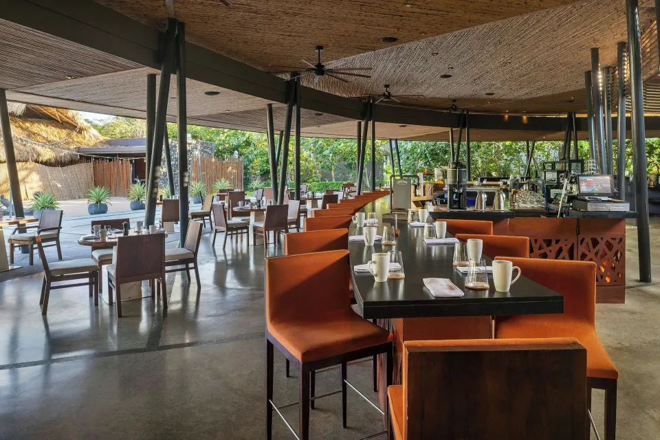 Open-plan dining with orange banquette seating and coffee service at El Mangroove Papagayo