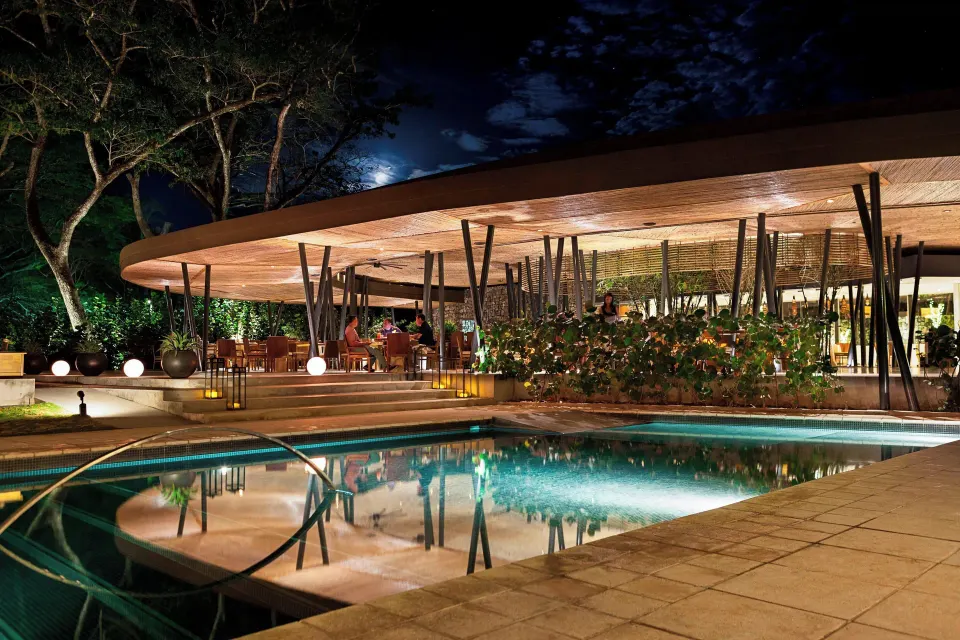 Night view of the resort pool with lit dining terrace beyond at El Mangroove Papagayo