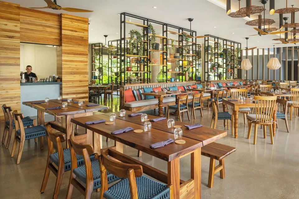 Spacious resort dining room with long communal tables and decorative shelving at El Mangroove Papagayo