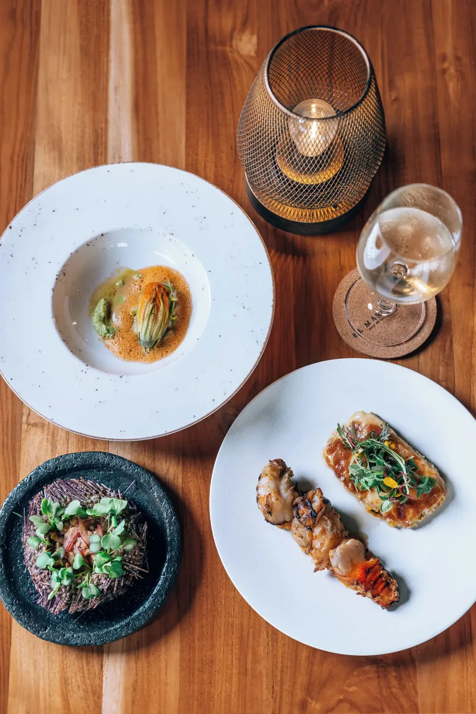 Three plated tasting dishes and a glass of wine on a wood table at El Mangroove Papagayo