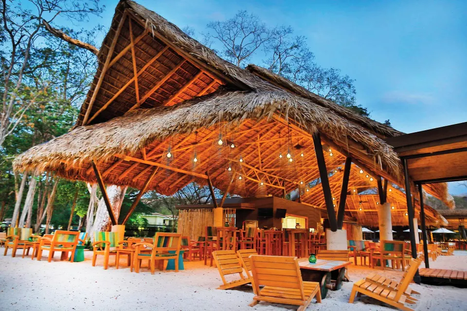 Thatched palapa bar with wooden seating on sand at El Mangroove Papagayo