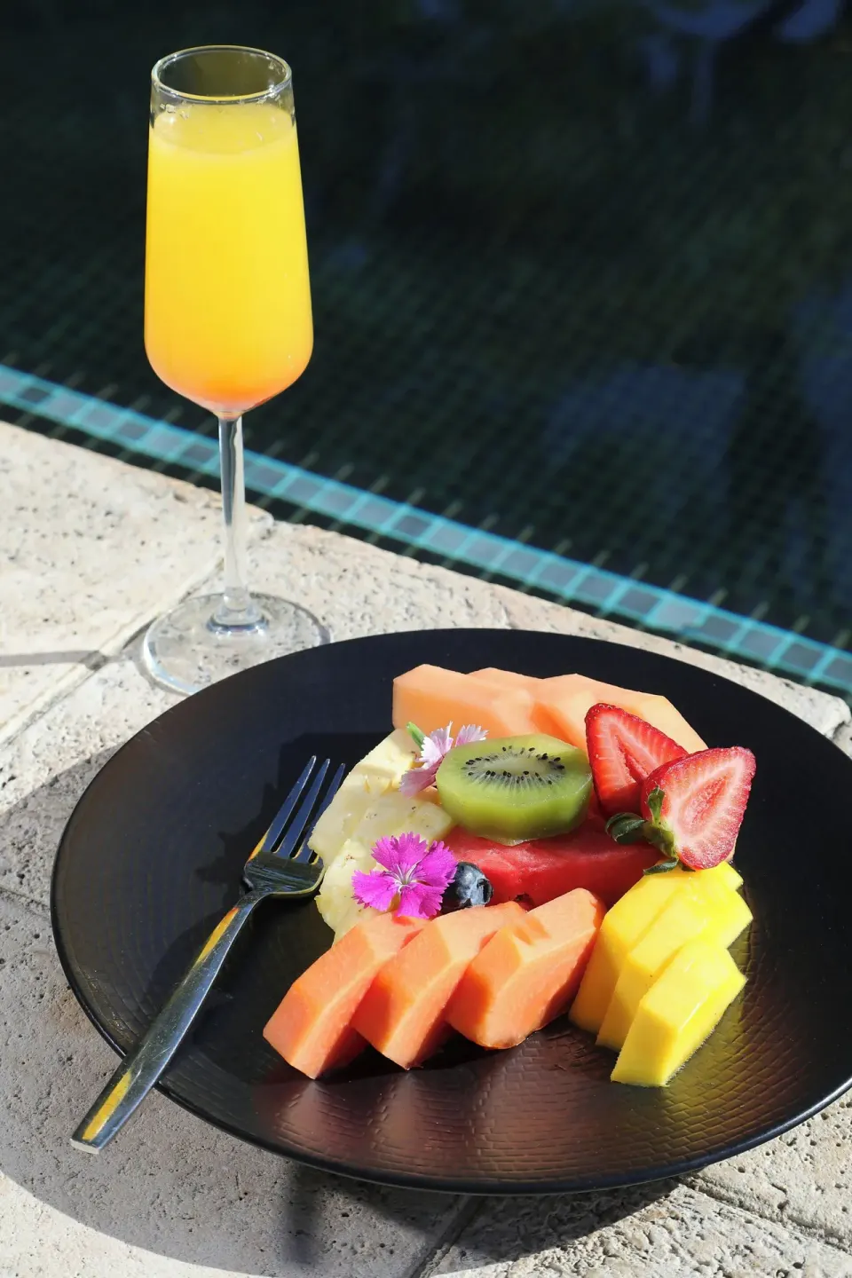 Plate of sliced tropical fruit and a mimosa by the pool at El Mangroove Papagayo