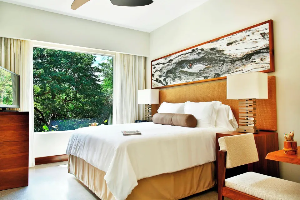Resort View Suite king bed and large window overlooking trees at El Mangroove Papagayo