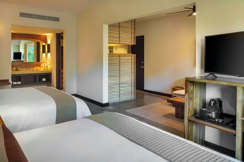 View from between two beds toward TV and bathroom area in a suite at El Mangroove Papagayo