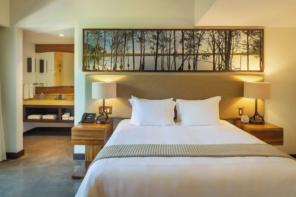 King bed framed by bedside lamps and nature artwork in a suite at El Mangroove Papagayo