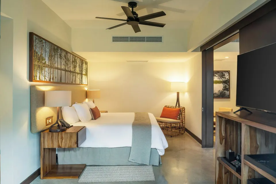 King bed with ceiling fan and wicker chair in a softly lit suite at El Mangroove Papagayo