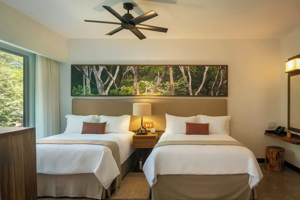 Front view of two beds with ceiling fan and forest artwork at El Mangroove Papagayo