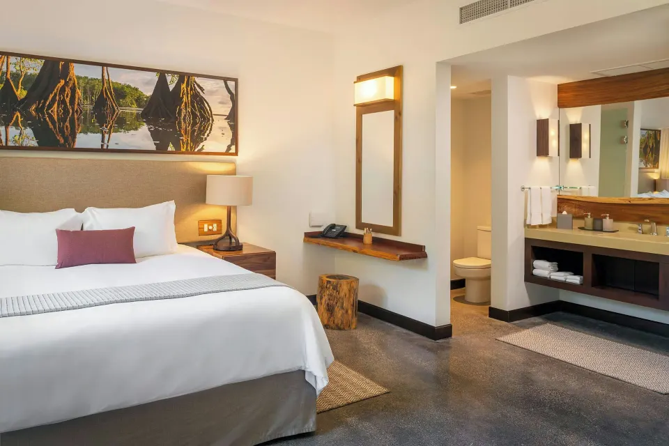 King bed with bedside lamp and view into bathroom vanity area at El Mangroove Papagayo