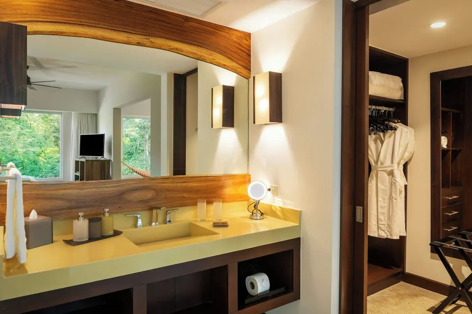 Bathroom sink and mirror with bedroom reflected in the glass in a suite at El Mangroove Papagayo