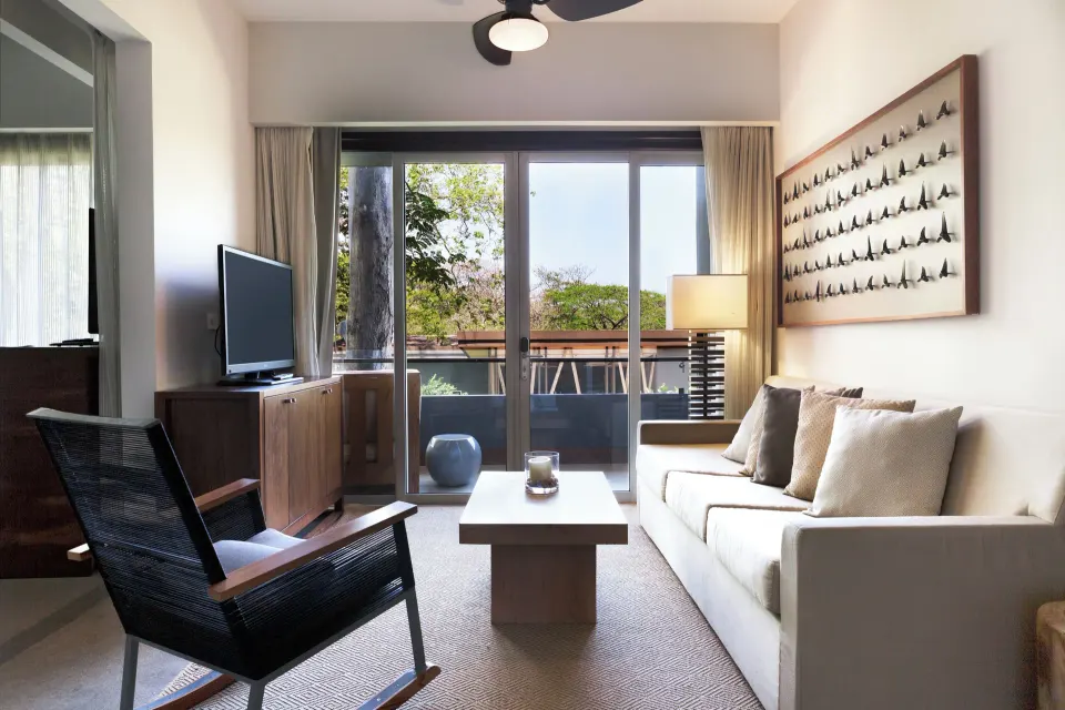 Living room view toward balcony with seating and TV in a Resort View Junior Suite at El Mangroove Papagayo