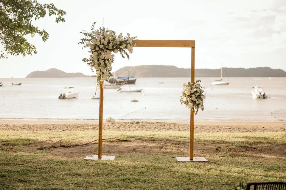 Simple wooden wedding arch on the beach with boats in the bay at El Mangroove Papagayo
