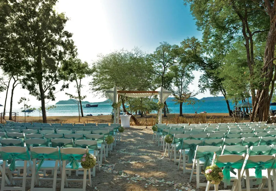 Outdoor beach wedding setup with rows of white chairs facing a seaside arch at El Mangroove Papagayo