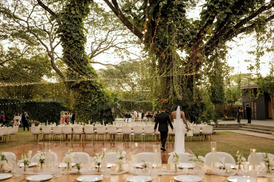 Bride and groom walking toward seating under large trees at El Mangroove Papagayo