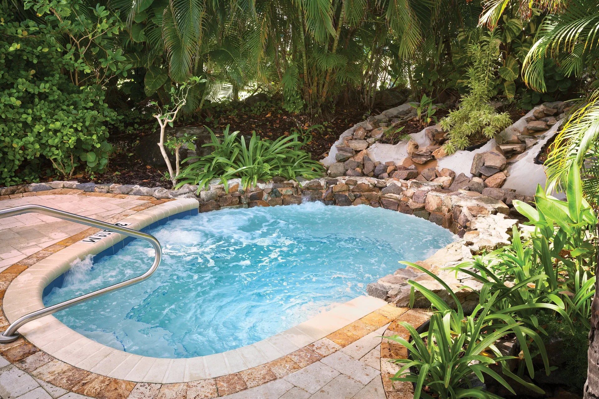 Small spa pool bordered by rocks and tropical plants at Elysian Beach Resort.