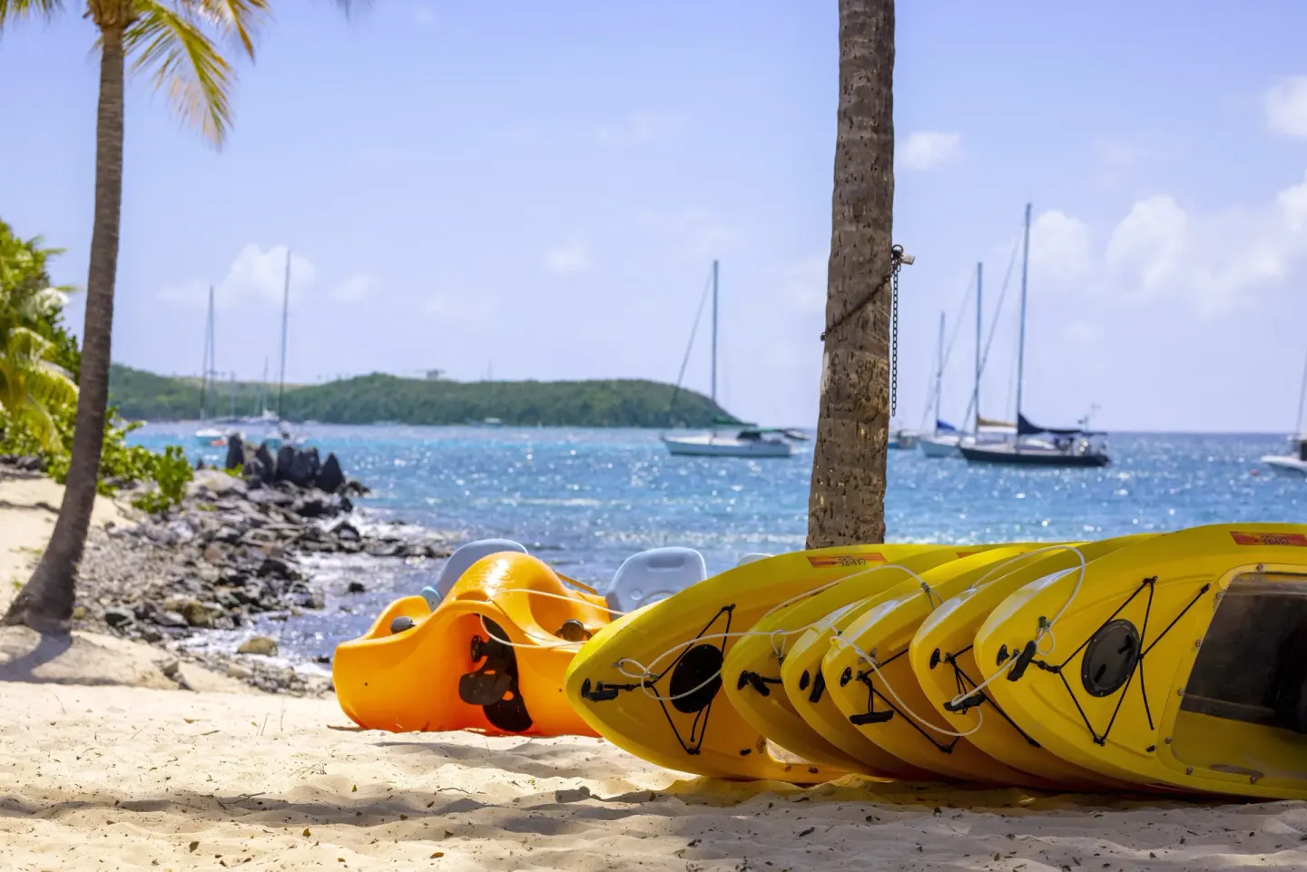 Yellow kayaks on the sand with sailboats offshore at Elysian Beach Resort.