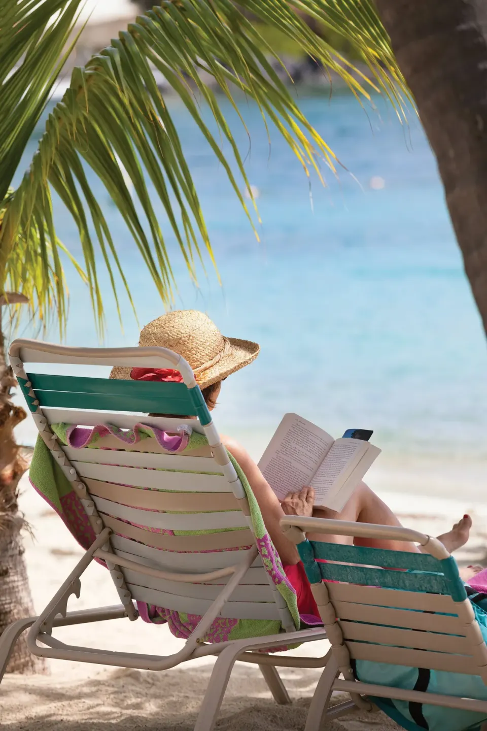 Guest reading in a beach chair under palm shade at Elysian Beach Resort.