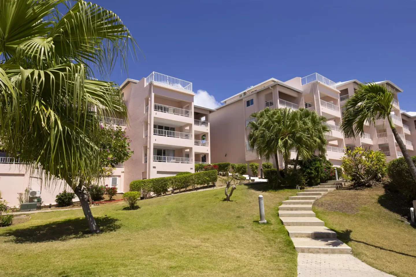 Pink resort buildings with balconies and lawn at Elysian Beach Resort.