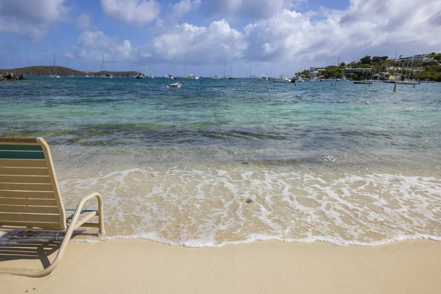 Shoreline lounge chair beside clear surf and anchored boats at Elysian Beach Resort.