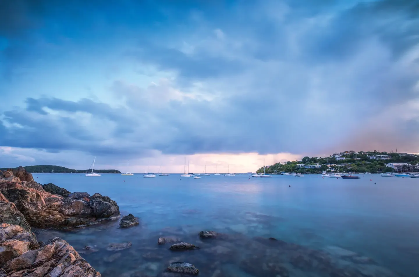 Rocky coast and calm bay beneath storm clouds at Elysian Beach Resort.