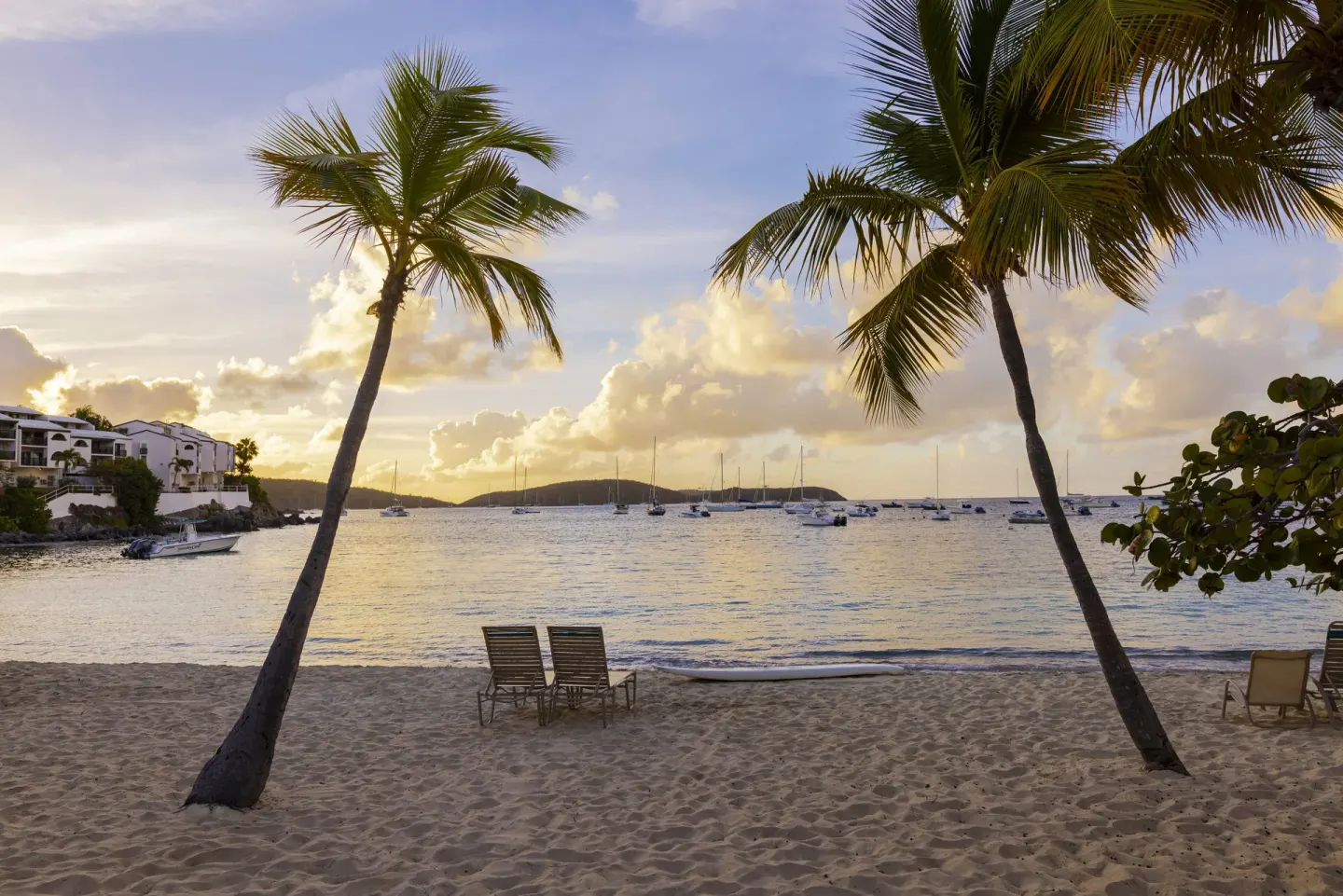 Sunset beach scene with two lounge chairs between palm trees at Elysian Beach Resort.