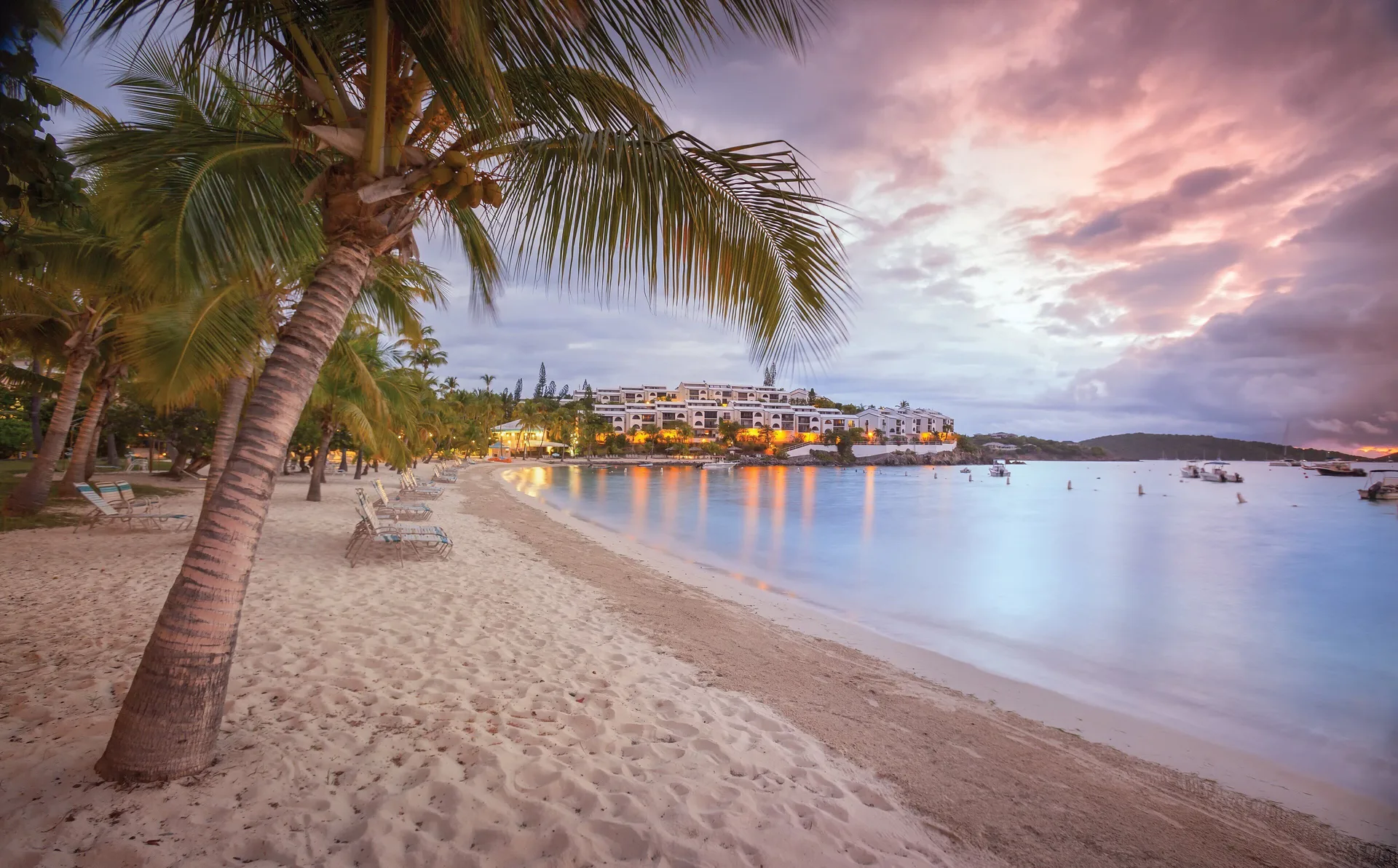 Palm-lined beach and resort buildings at sunset at Elysian Beach Resort.