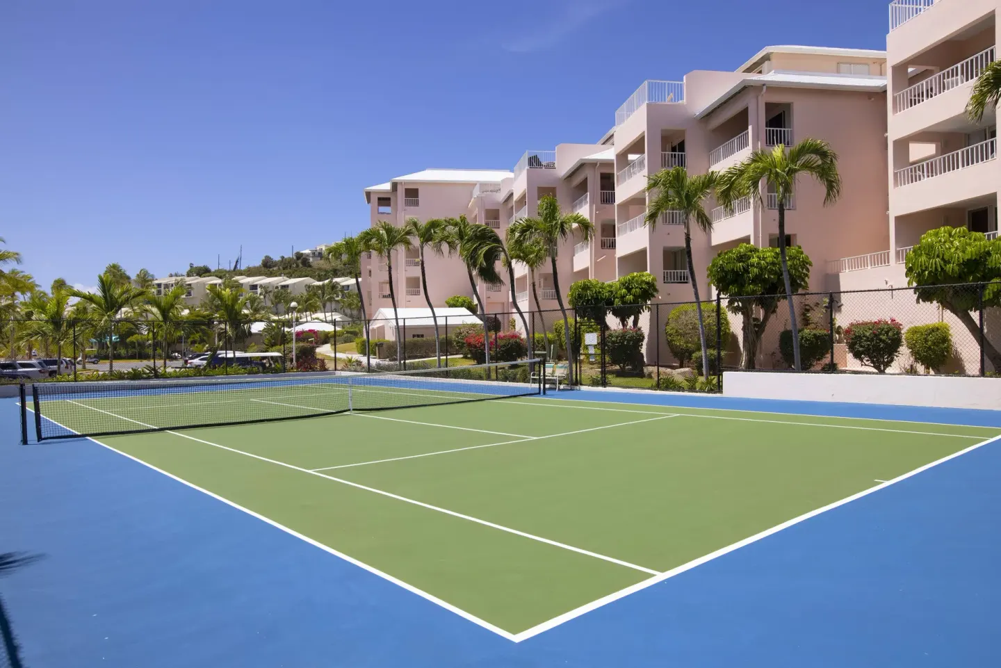 Tennis court beside resort buildings and palms at Elysian Beach Resort.