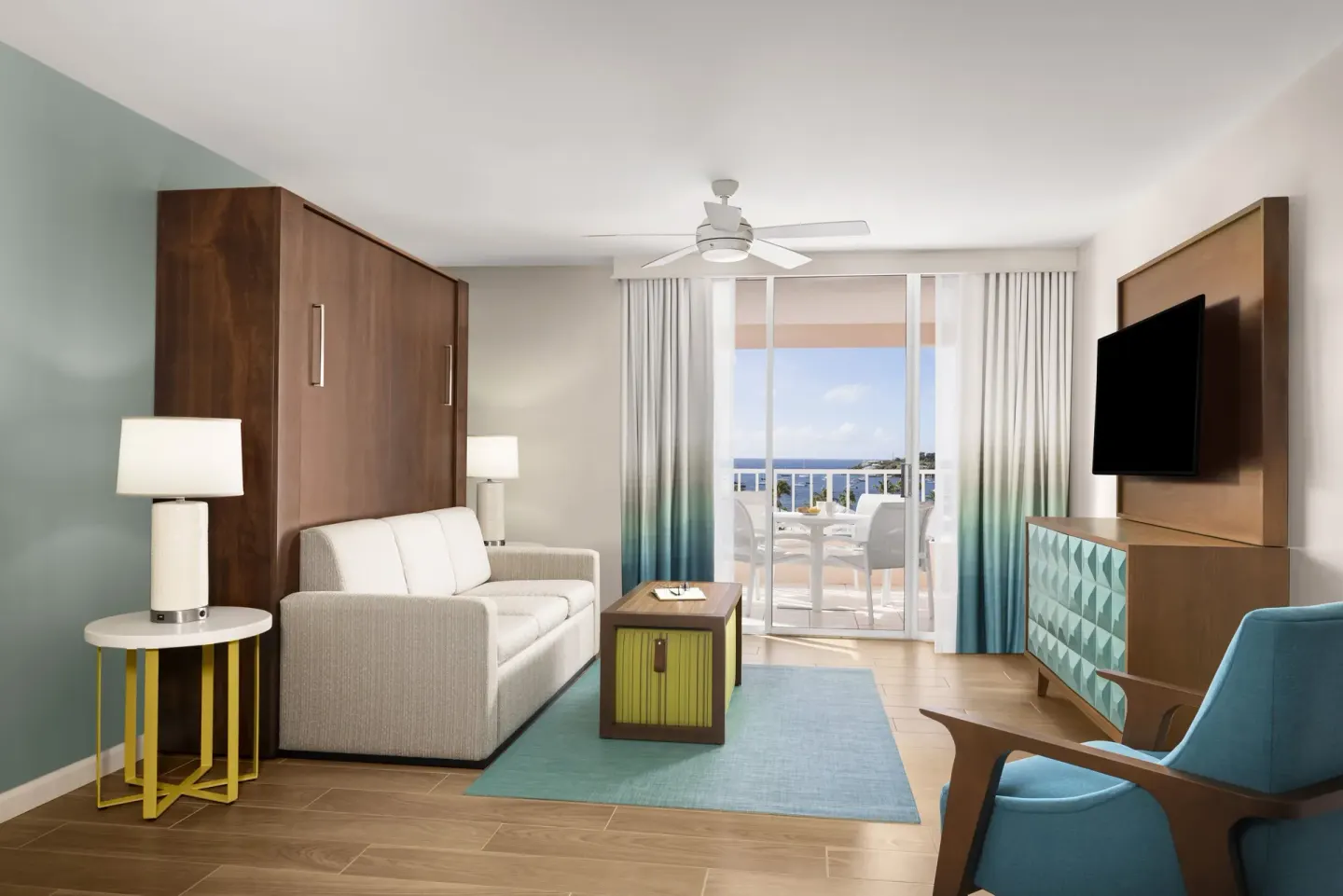 Comfort Studio living area with sofa, TV, balcony doors, and ocean view at Elysian Beach Resort.