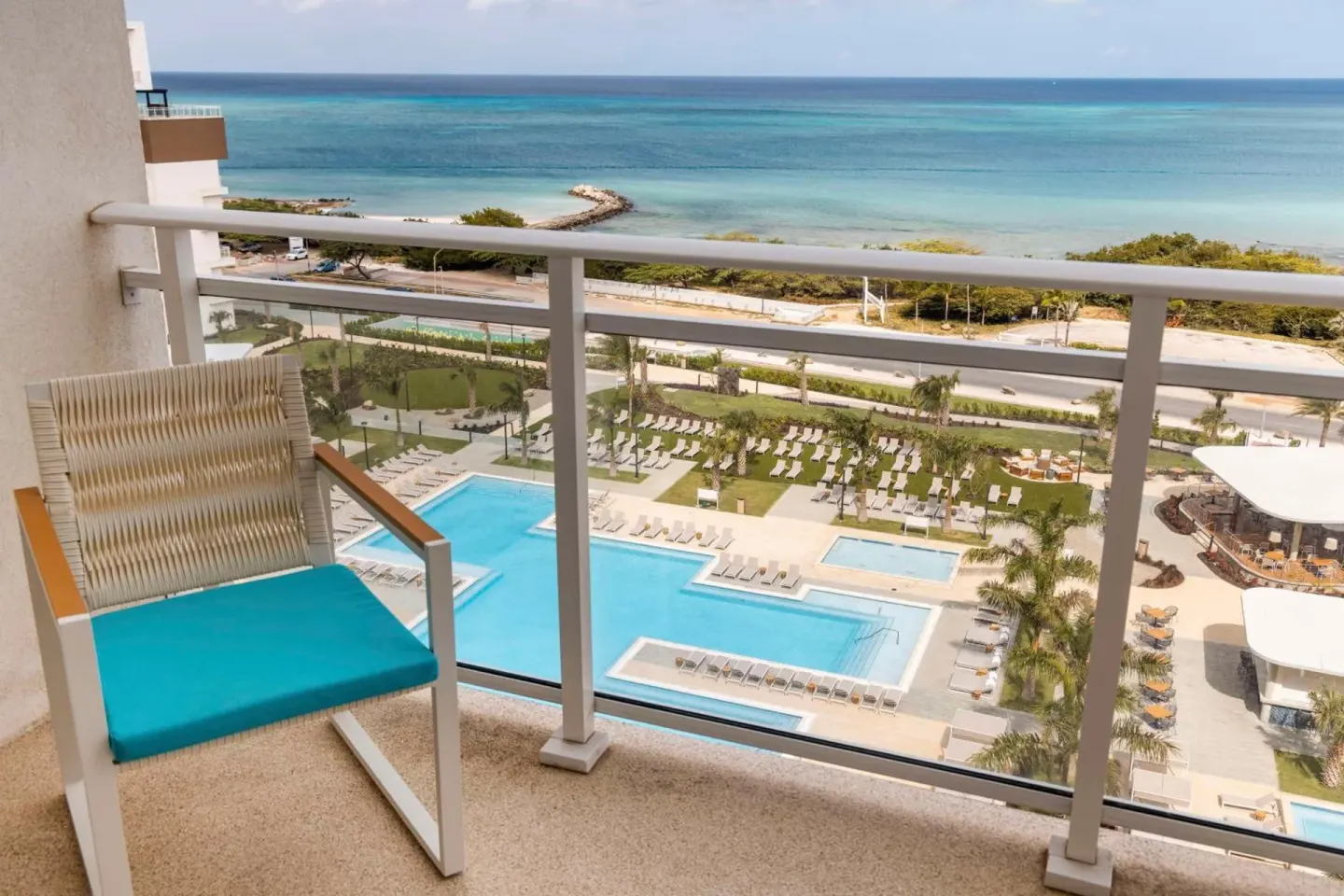 Balcony chair overlooking pools and the ocean at Embassy Suites Aruba Beach Resort.