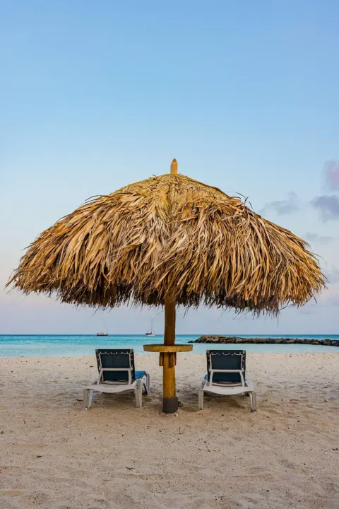 Beach palapa and two lounge chairs by the water at Embassy Suites Aruba Beach Resort.