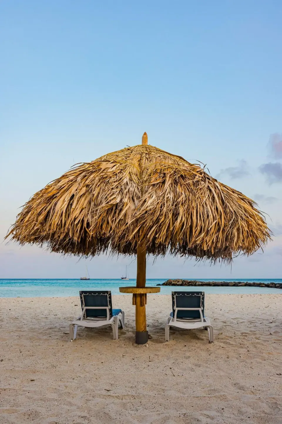 Beach palapa and two lounge chairs by the water at Embassy Suites Aruba Beach Resort.