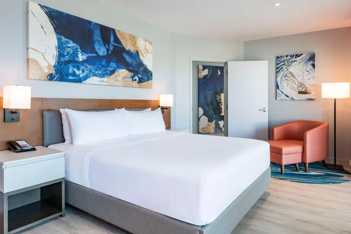 Guest room with king bed, artwork and armchair at Embassy Suites Aruba Beach Resort.