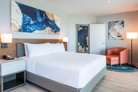 Guest room with king bed, artwork and armchair at Embassy Suites Aruba Beach Resort.
