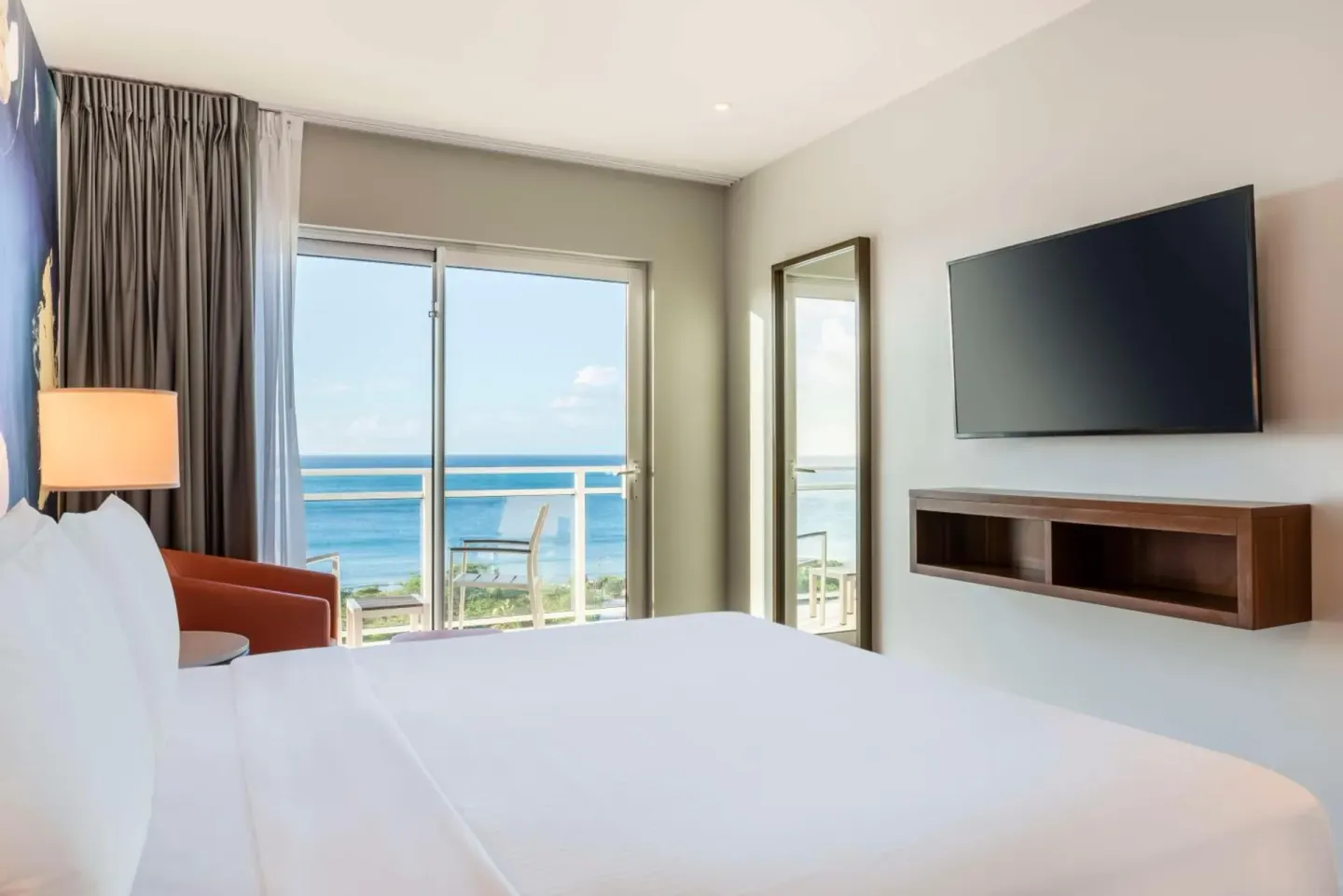 Guest room with bed, wall-mounted TV, balcony, and ocean view at Embassy Suites Aruba Beach Resort.