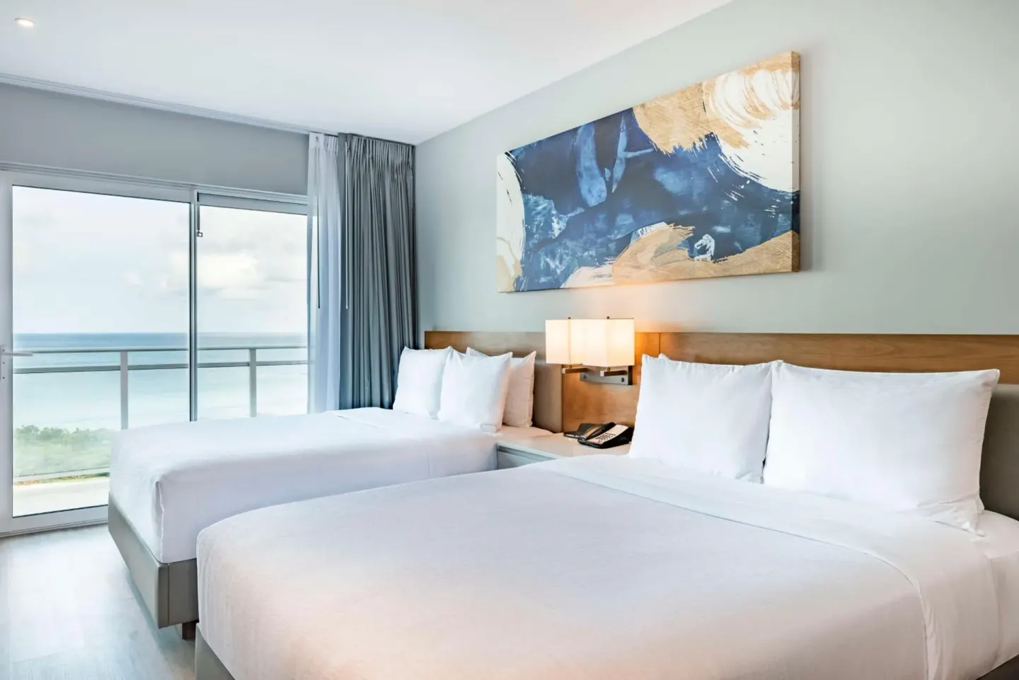 Guest room with two queen beds and ocean-facing balcony at Embassy Suites Aruba Beach Resort.