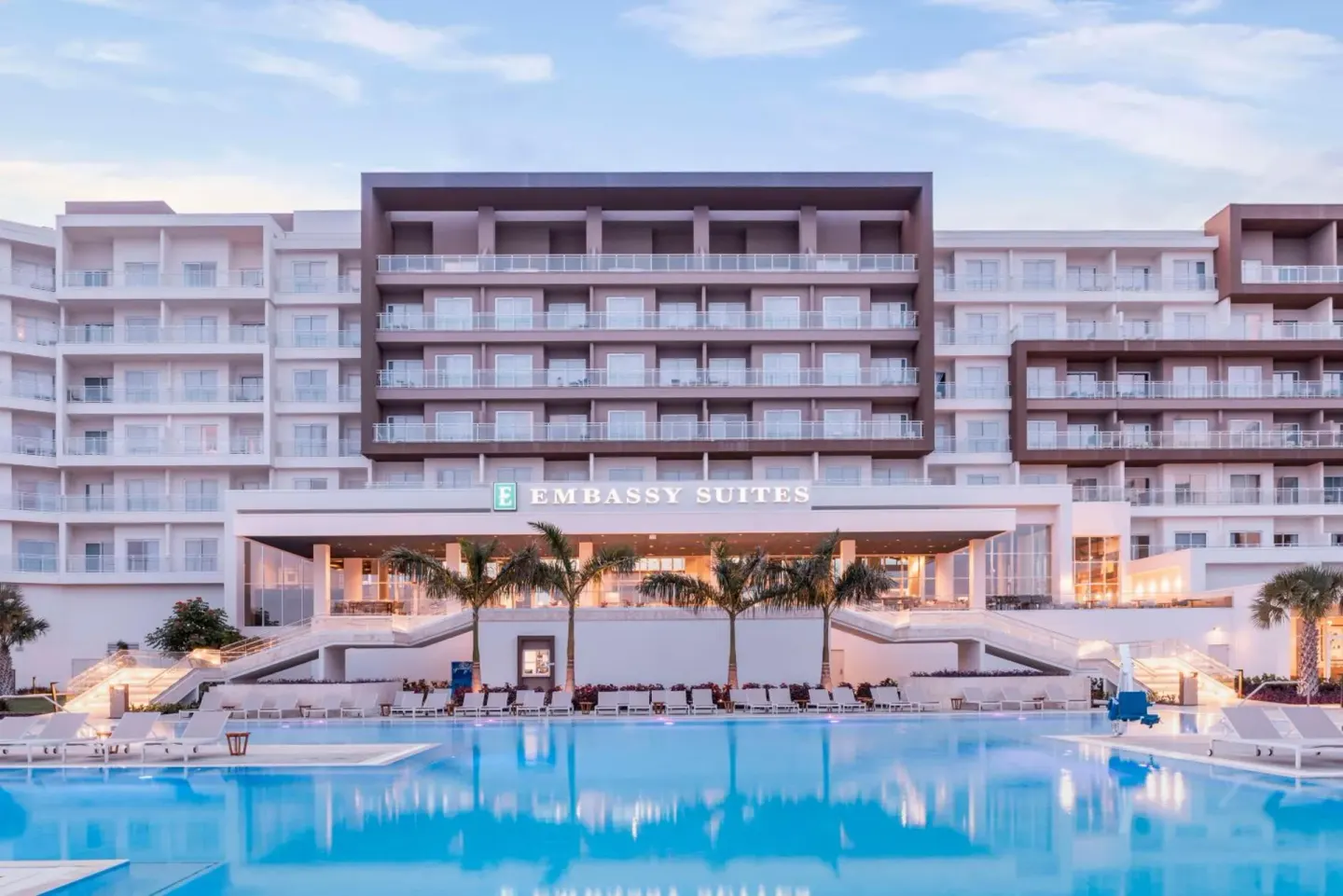Pool and main building facade at Embassy Suites Aruba Beach Resort at dusk.