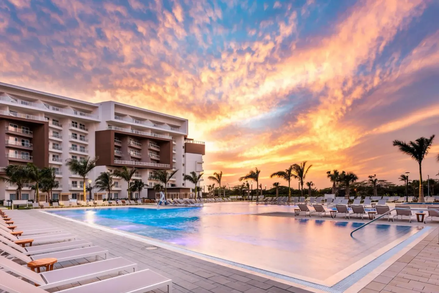 Large resort pool and lounge chairs at sunset at Embassy Suites Aruba Beach Resort.