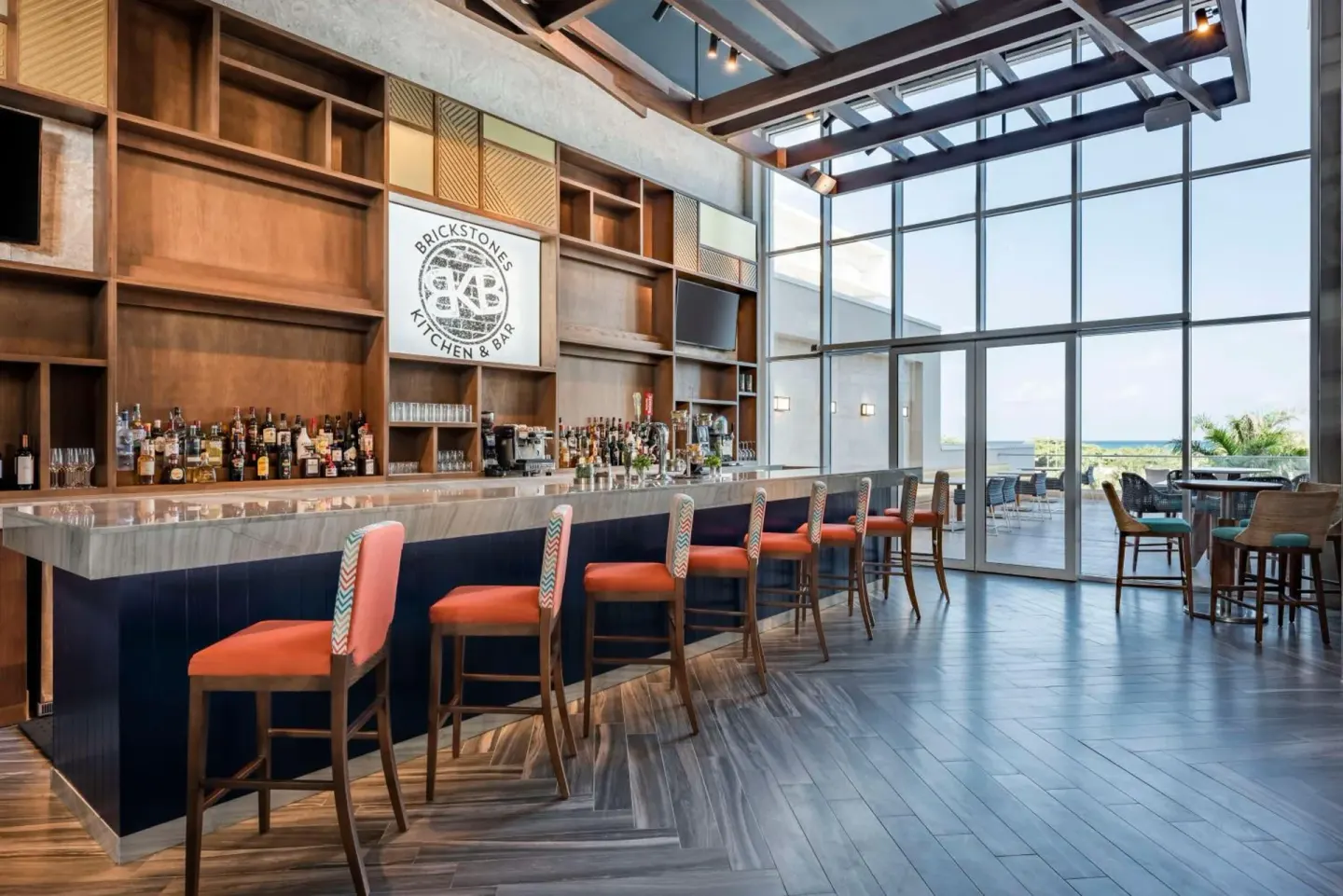 Brickstones bar with stools and ocean-facing windows at Embassy Suites Aruba Beach Resort.