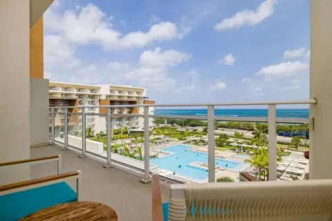 Top-floor balcony with pool, resort grounds, and ocean at Embassy Suites Aruba Beach Resort.