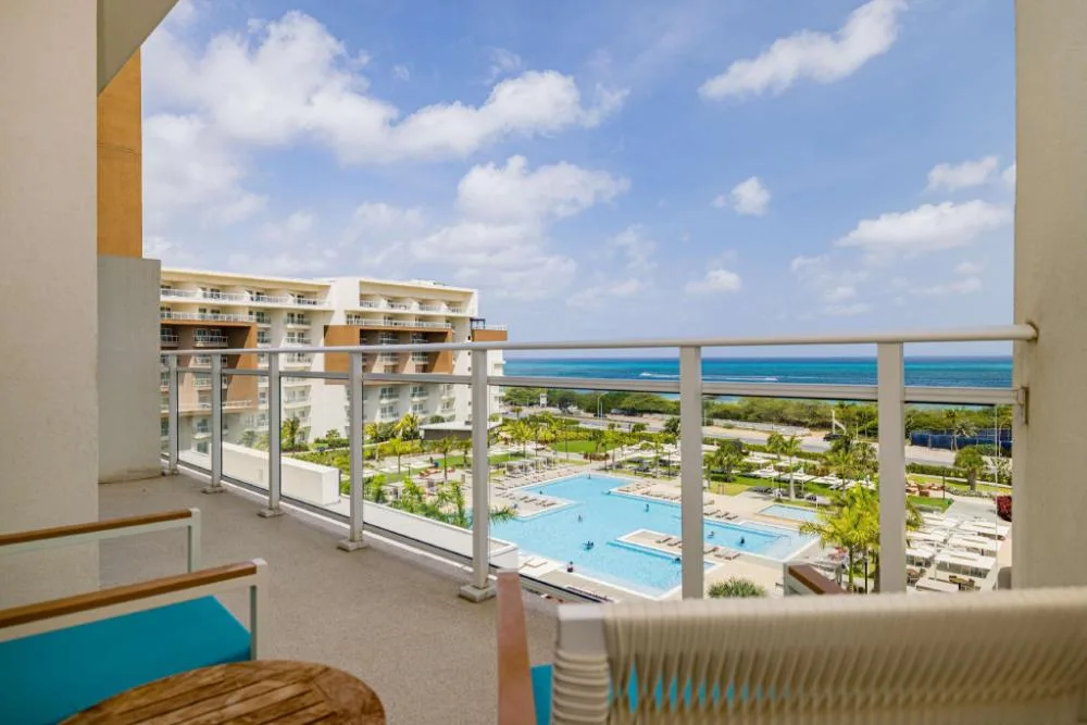 Top-floor balcony with pool, resort grounds, and ocean at Embassy Suites Aruba Beach Resort.